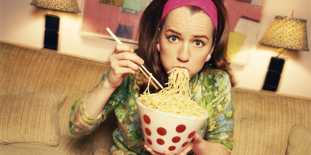 Woman eating noodles, sitting on sofa, portrait