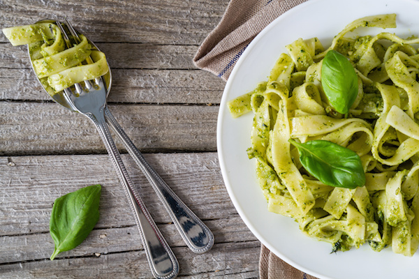 Pesto pasta on white plate, top view, rustic wood background